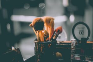 Assorted makeup brushes stand upright in a dark brass container. Photo by Raphael Lovaski on Unsplash.