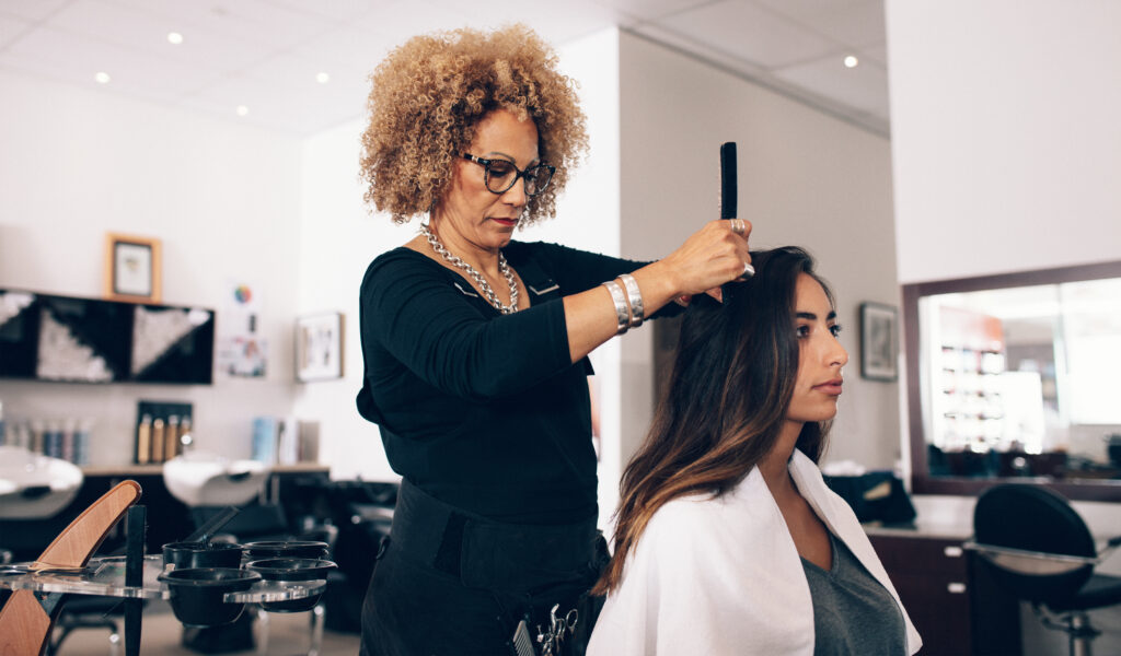 Female hair stylist working on a woman 's hair. Woman hairdresser serving her customer at the salon.